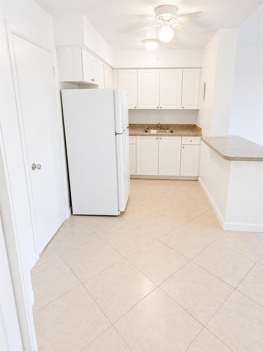 A kitchen features white cabinets, a white refrigerator, tan countertops, and light-colored tile flooring — 1960 NE 48th Street # 7, Pompano Beach FL 33064, POMPANO BEACH, FL