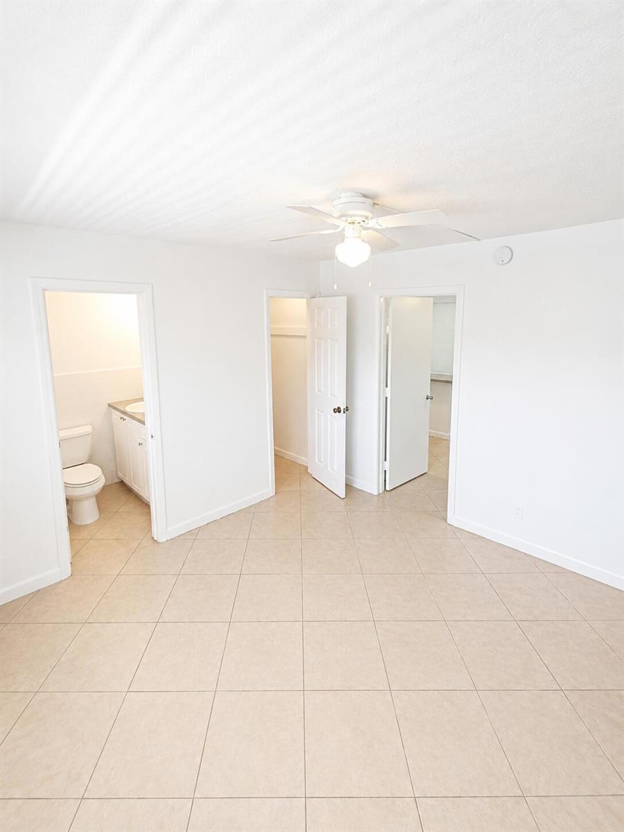 A room with beige tile flooring, a ceiling fan, and three open doorways — 1960 NE 48th Street # 7, Pompano Beach FL 33064, POMPANO BEACH, FL