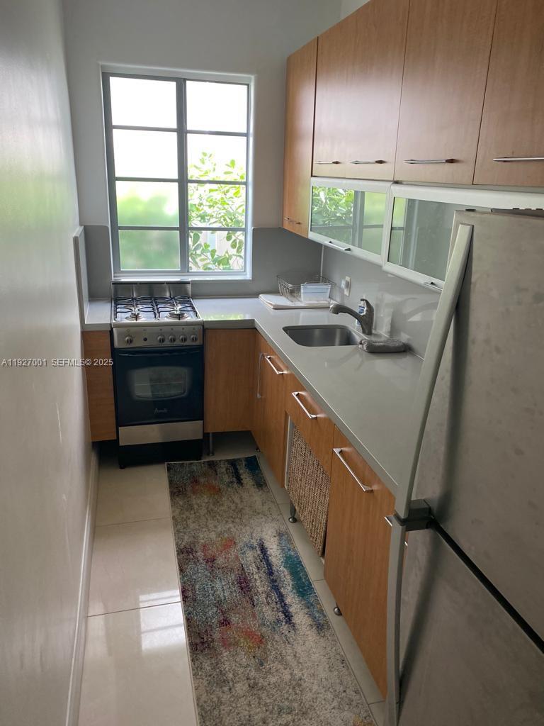 A galley kitchen features light wood cabinets, stainless steel appliances, and a window above the stove — 526 15 ST # 2, Miami Beach FL 33139, MIAMI BEACH, FL