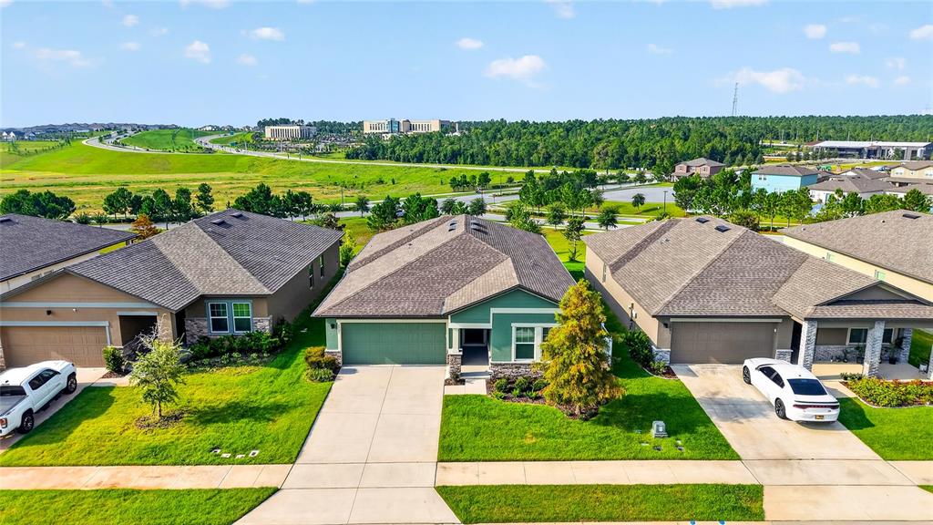 An aerial view shows three suburban houses with driveways and lawns under a blue sky — 1785 SUNDANCE CHASE ROAD, MINNEOLA, FL