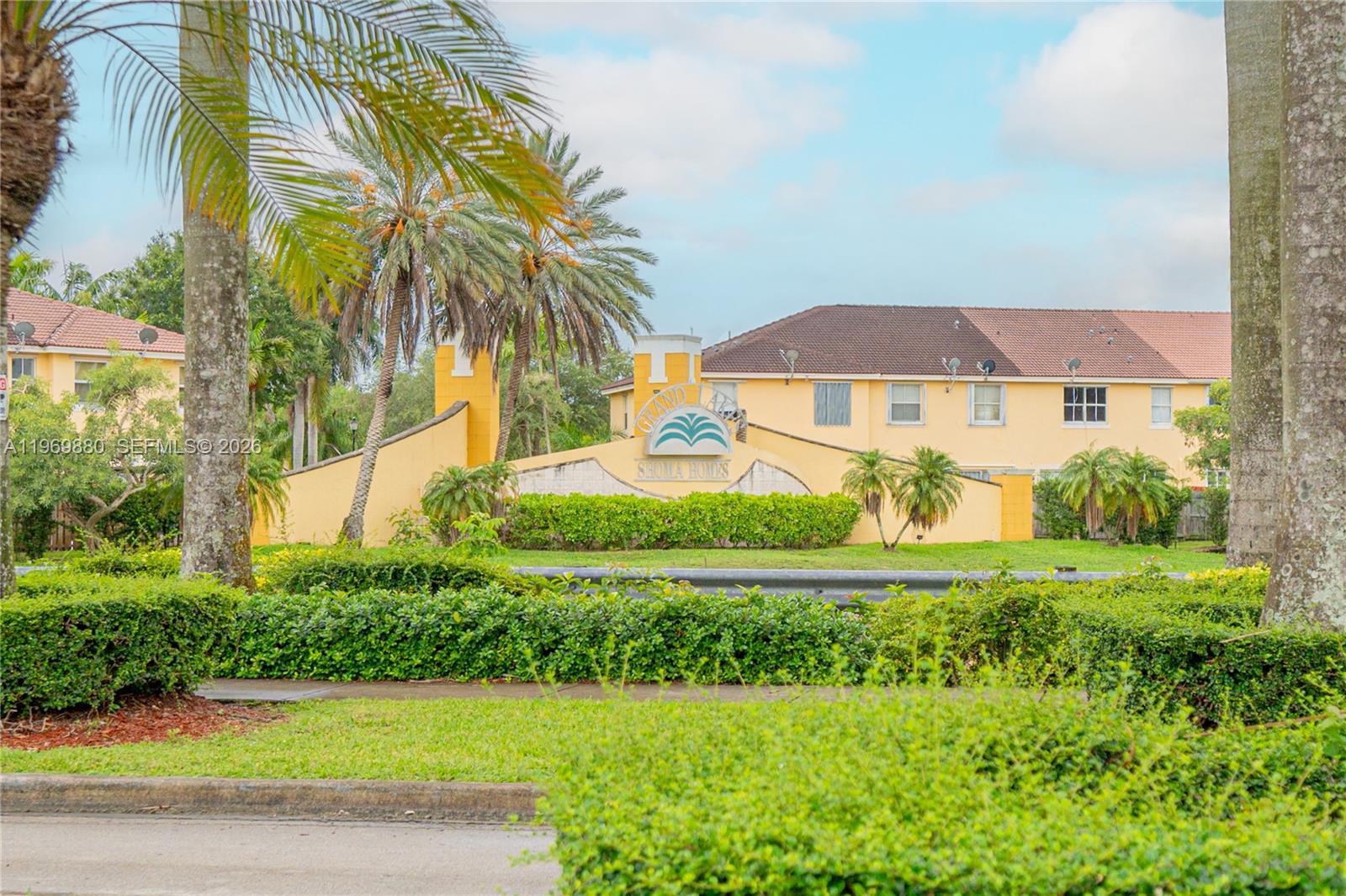The exterior of a residential community features a yellow wall with a palm tree logo — 14964 SW 8 LN, Miami FL 33194, MIAMI, FL