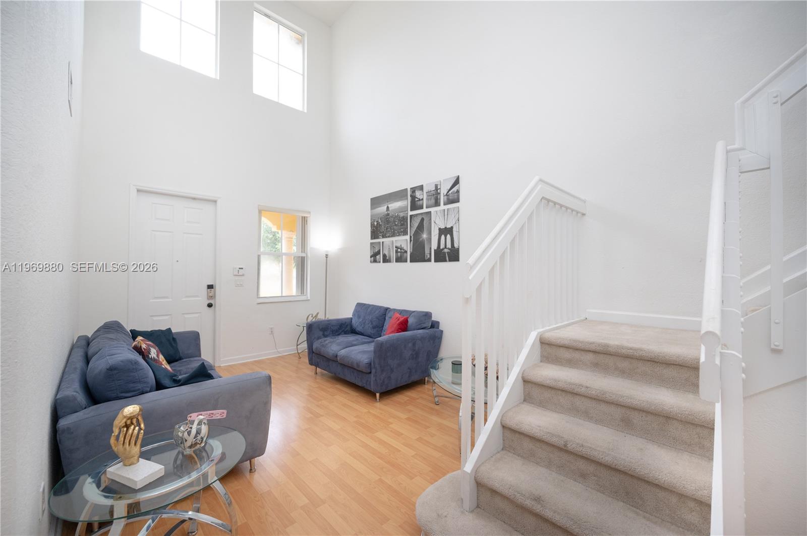A living room features high ceilings, light wood flooring, two blue sofas, and a staircase — 14964 SW 8 LN, Miami FL 33194, MIAMI, FL