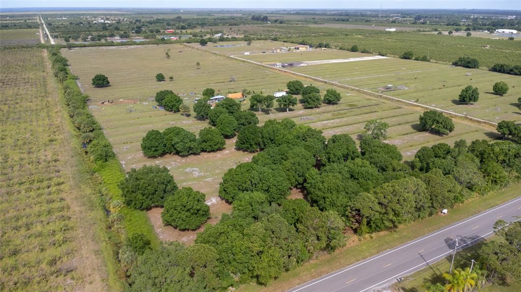 An aerial view shows a large, flat, grassy lot with scattered trees and a paved road — 11525 138TH AVENUE, FELLSMERE, FL