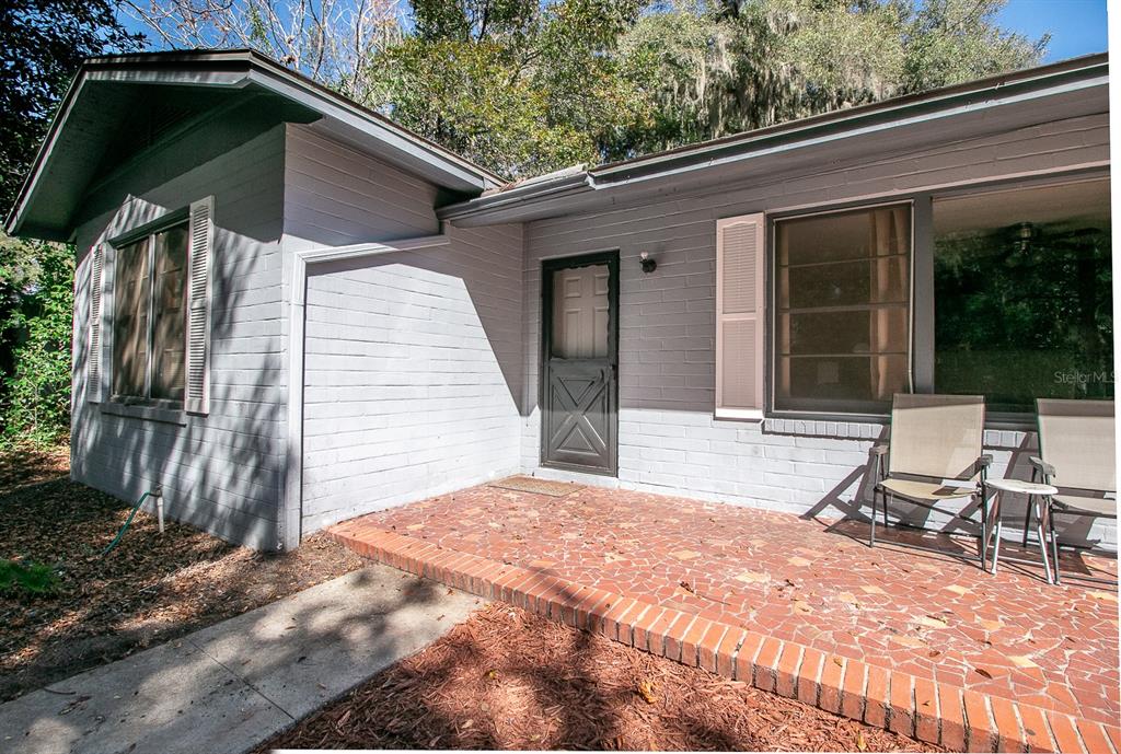 A gray painted brick house exterior features a red brick patio and a front door — 2016 NW 7TH PLACE, GAINESVILLE, FL