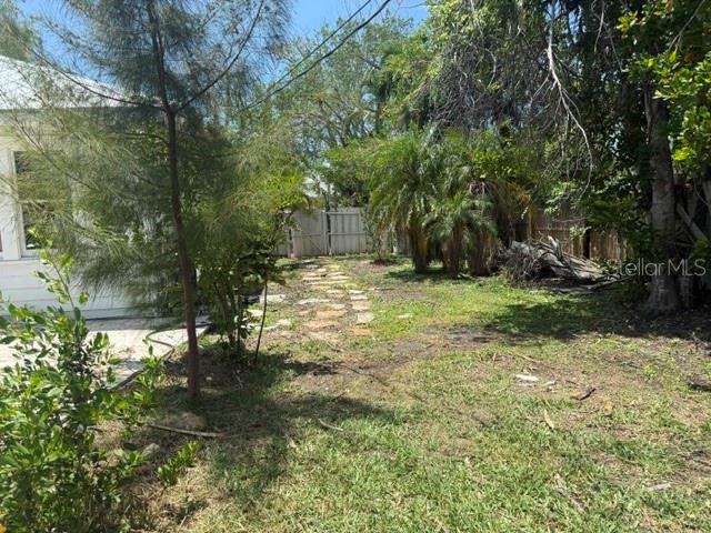 A backyard features a stone path leading toward a white fence and lush green trees — 617 SIESTA DRIVE, SARASOTA, FL