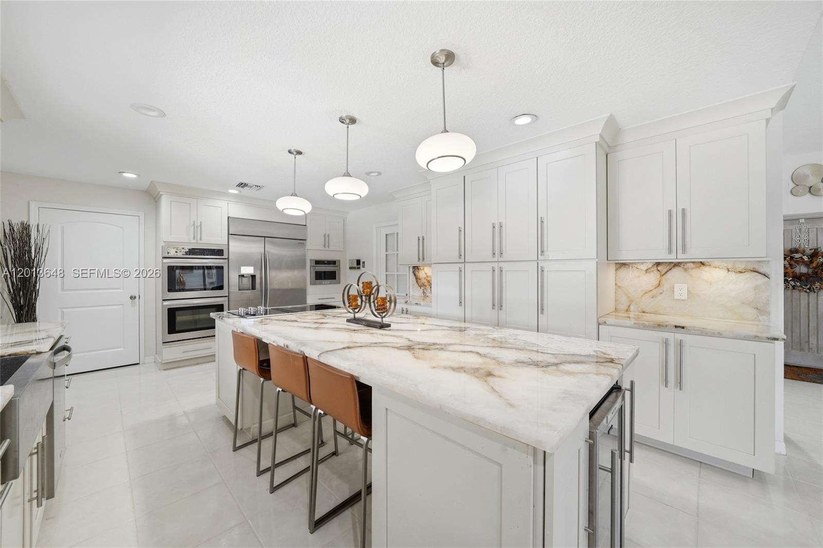 A modern white kitchen features a large marble island with three brown leather bar stools — 15130 SW 164th Ter, Miami FL 33187, MIAMI, FL