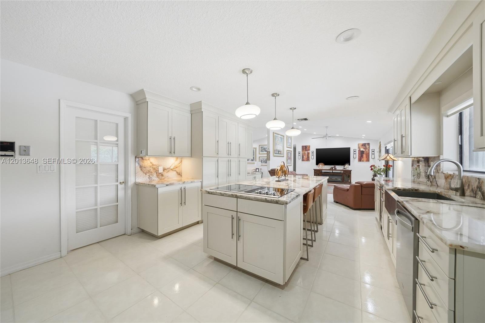 A modern kitchen features light-colored cabinetry, a large marble-topped island, and tile flooring — 15130 SW 164th Ter, Miami FL 33187, MIAMI, FL
