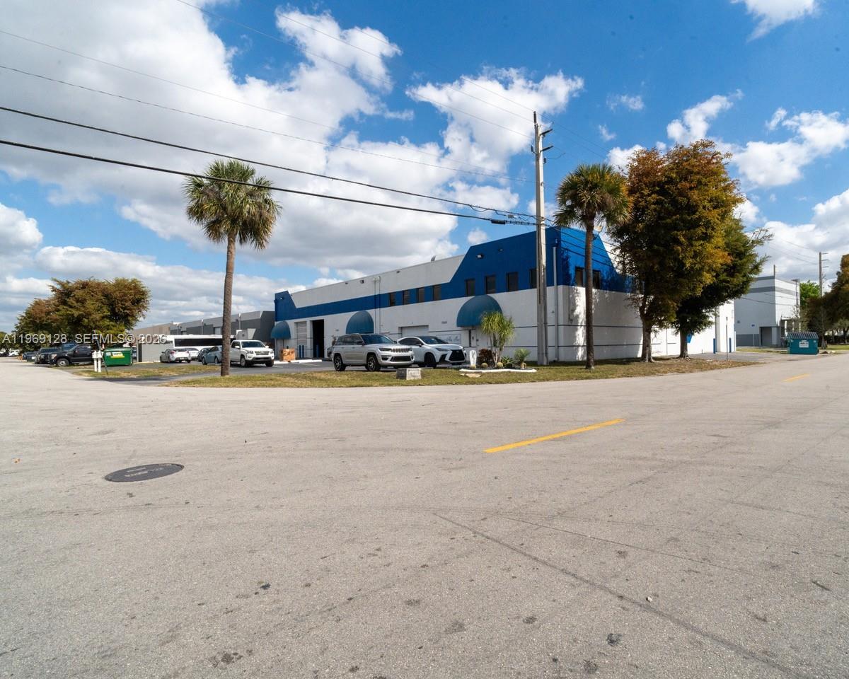 A low-rise industrial building with blue accents and palm trees sits beside a paved road — 7801 W 25th Ct, Hialeah FL 33016, HIALEAH, FL