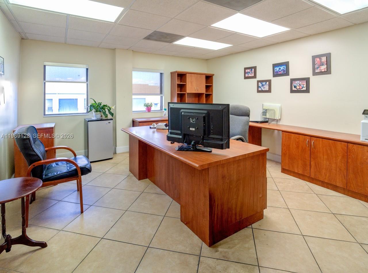An office features a wooden desk, a computer monitor, tile flooring, and built-in cabinetry — 7801 W 25th Ct, Hialeah FL 33016, HIALEAH, FL