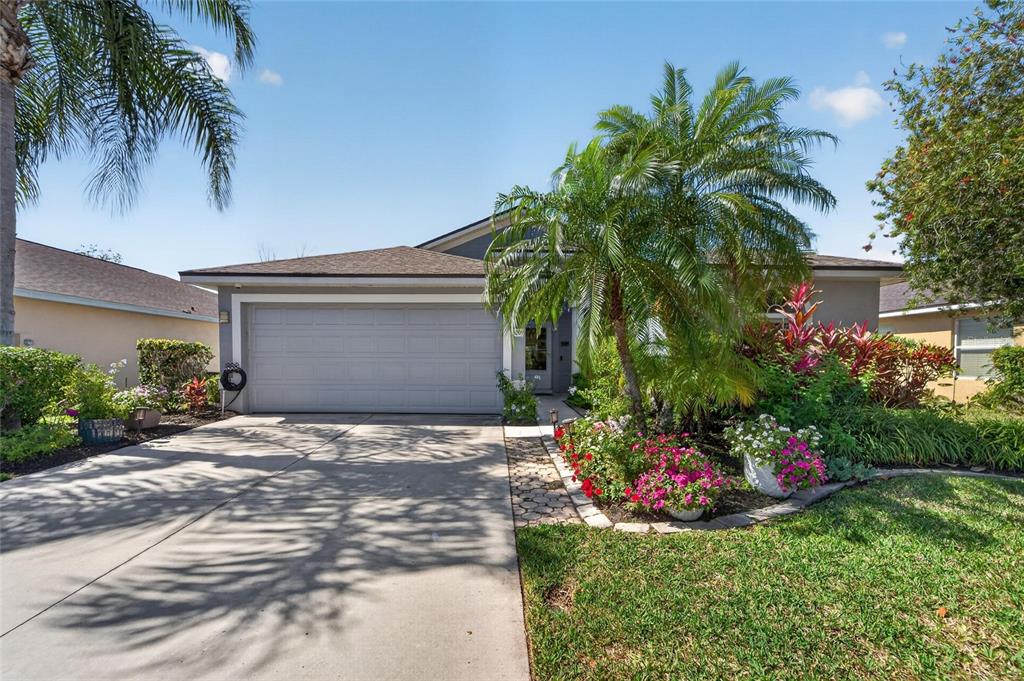 A single-story house features a gray garage, a palm tree, and a landscaped front garden — 5209 LANSDOWNE WAY, PALMETTO, FL