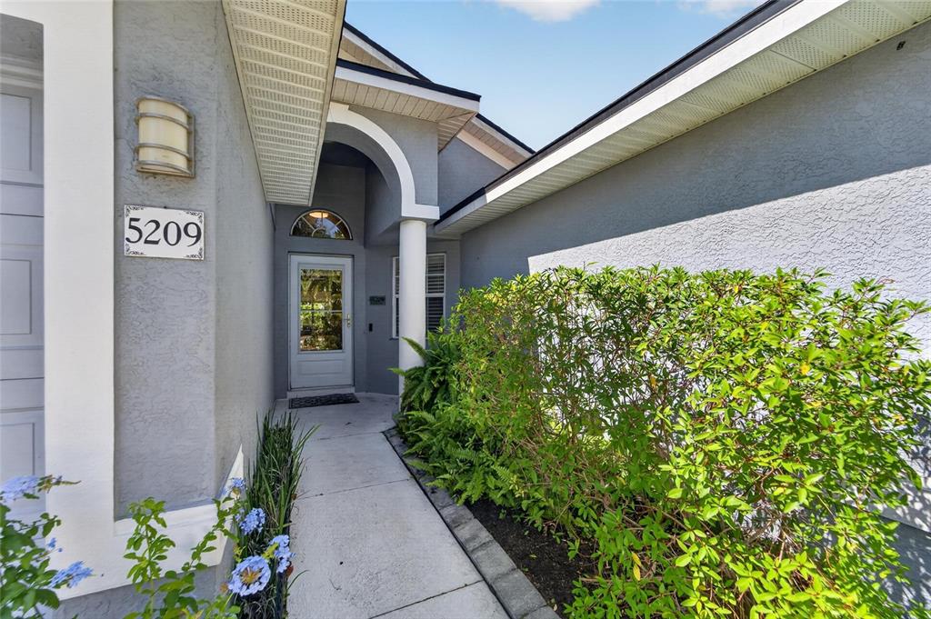 A concrete walkway leads to the front entrance of a house with gray stucco walls — 5209 LANSDOWNE WAY, PALMETTO, FL