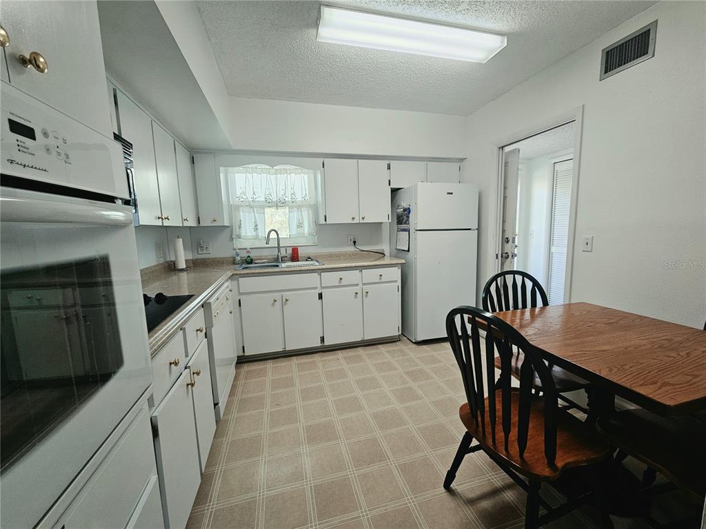 A kitchen with white cabinets, white appliances, a dining table, and checkered flooring — 2292 COSTA RICAN DRIVE UNIT 24, CLEARWATER, FL