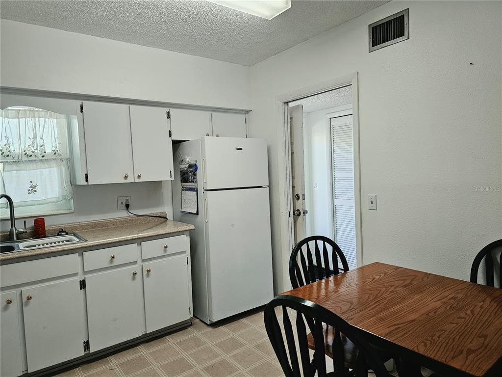 A kitchen features white cabinets, a white refrigerator, and a wooden dining table — 2292 COSTA RICAN DRIVE UNIT 24, CLEARWATER, FL