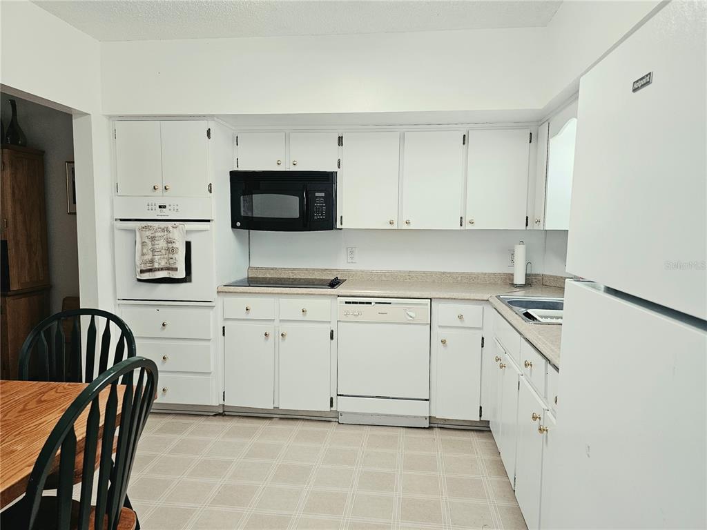 A kitchen features white cabinets, a black microwave, white appliances, and a laminate countertop — 2292 COSTA RICAN DRIVE UNIT 24, CLEARWATER, FL