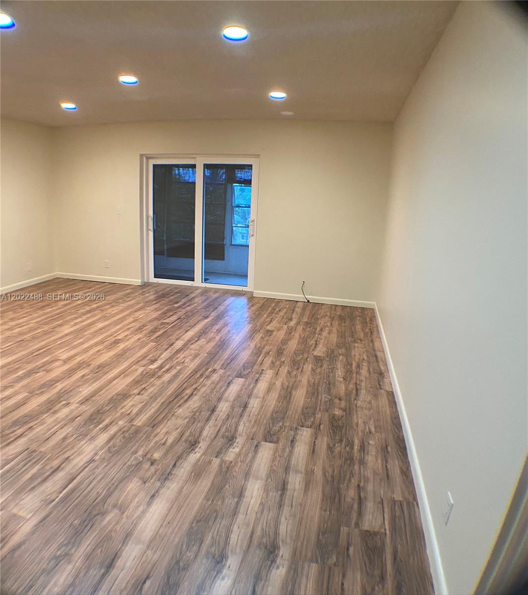 An empty room features wood-look flooring, recessed lighting, and a sliding glass door — 2061 NW 47th Ter # 302, Lauderhill FL 33313, LAUDERHILL, FL