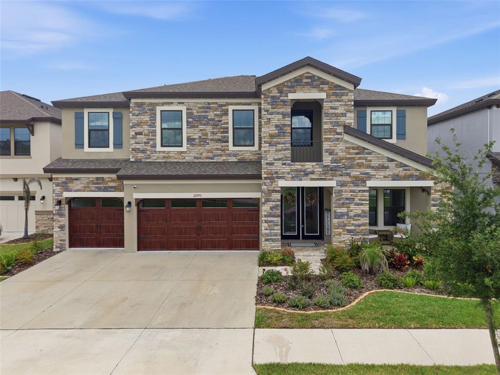 A two-story house features a stone facade, a three-car garage, and a covered front entryway — 12970 STEED TRACE LOOP, LITHIA, FL