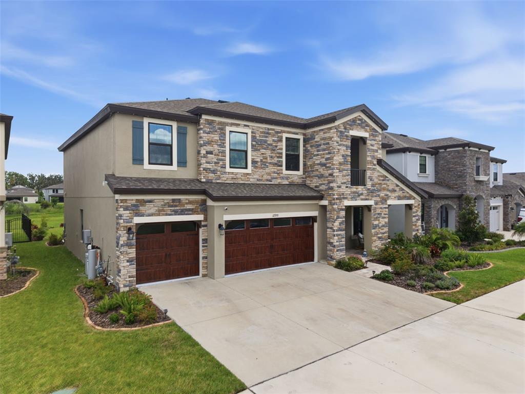 A two-story house with a stone facade, a three-car garage, and a concrete driveway — 12970 STEED TRACE LOOP, LITHIA, FL