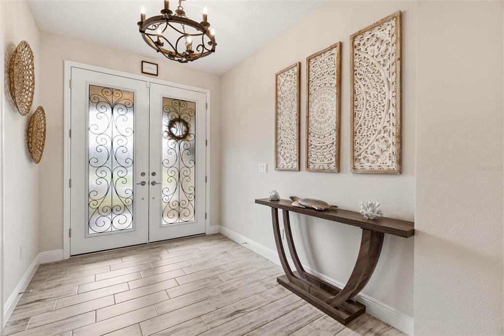 An entryway features double glass-paneled doors, a wooden console table, and three decorative wall panels — 12970 STEED TRACE LOOP, LITHIA, FL