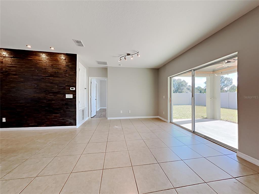 A living area features large beige floor tiles, a dark wood-paneled accent wall, and sliding doors — 434 SALAMANCA ROAD, DAVENPORT, FL