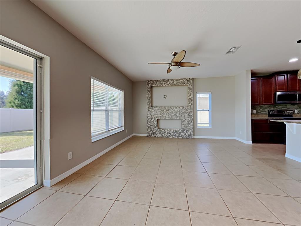 A living room with tile floors, a stone-accented fireplace wall, and a ceiling fan — 434 SALAMANCA ROAD, DAVENPORT, FL