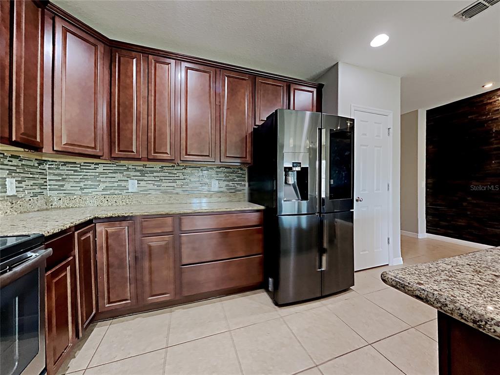 A kitchen features dark wood cabinets, granite countertops, a tiled backsplash, and a stainless refrigerator — 434 SALAMANCA ROAD, DAVENPORT, FL