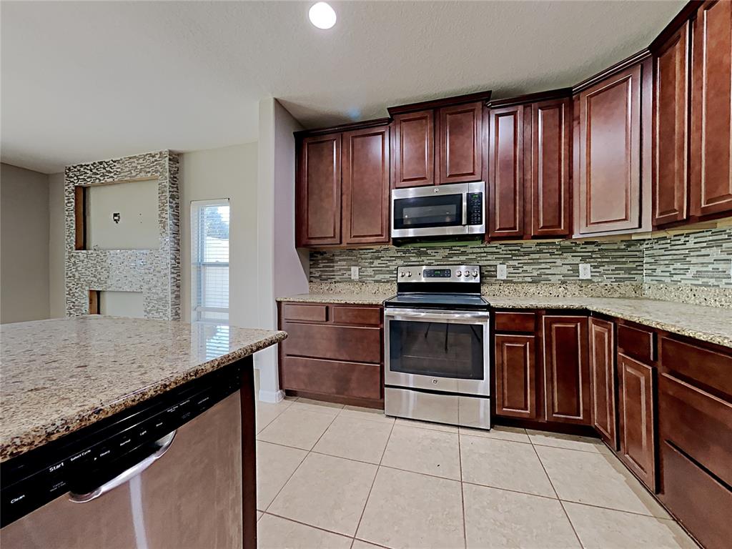 A kitchen features dark wood cabinets, granite countertops, stainless steel appliances, and tile flooring — 434 SALAMANCA ROAD, DAVENPORT, FL