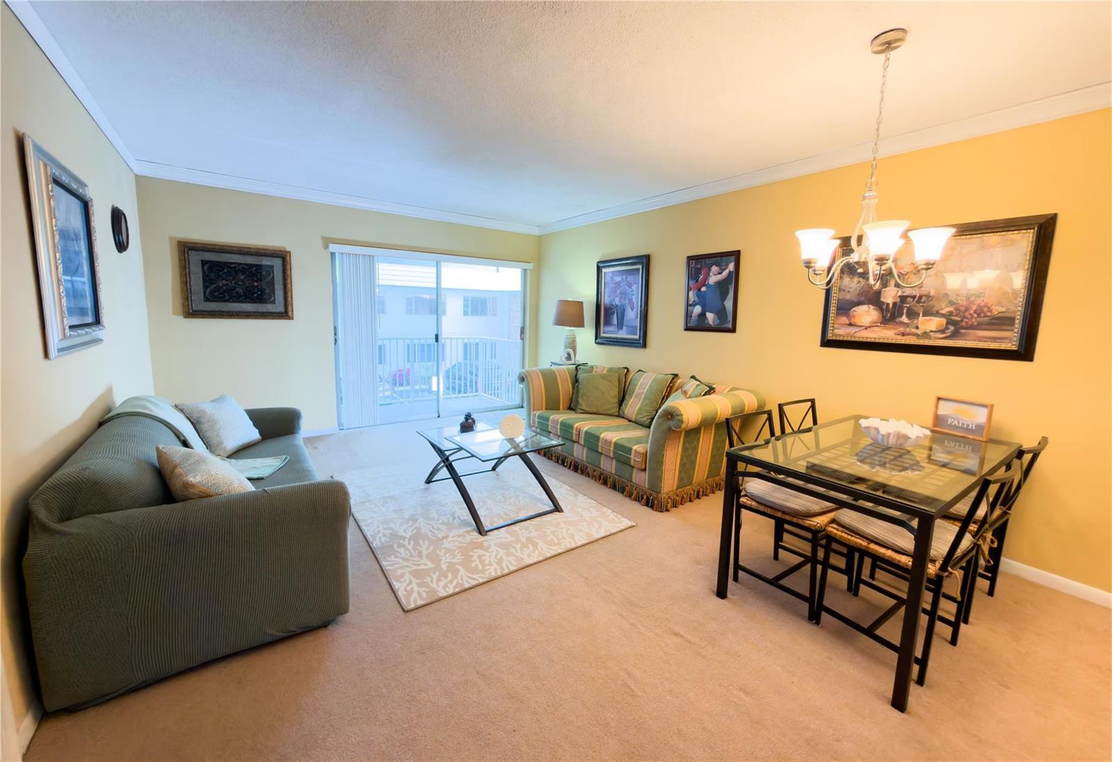 A living and dining room with yellow walls, beige carpet, and a glass-topped dining set — 412 S Cypress Road # 225, Pompano Beach FL 33060, POMPANO BEACH, FL