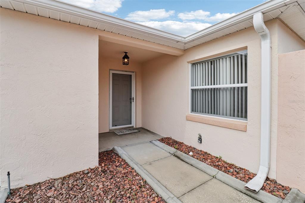 A concrete walkway leads to the front entrance of a house with light-colored stucco walls — 914 MENDOZA BOULEVARD, LADY LAKE, FL