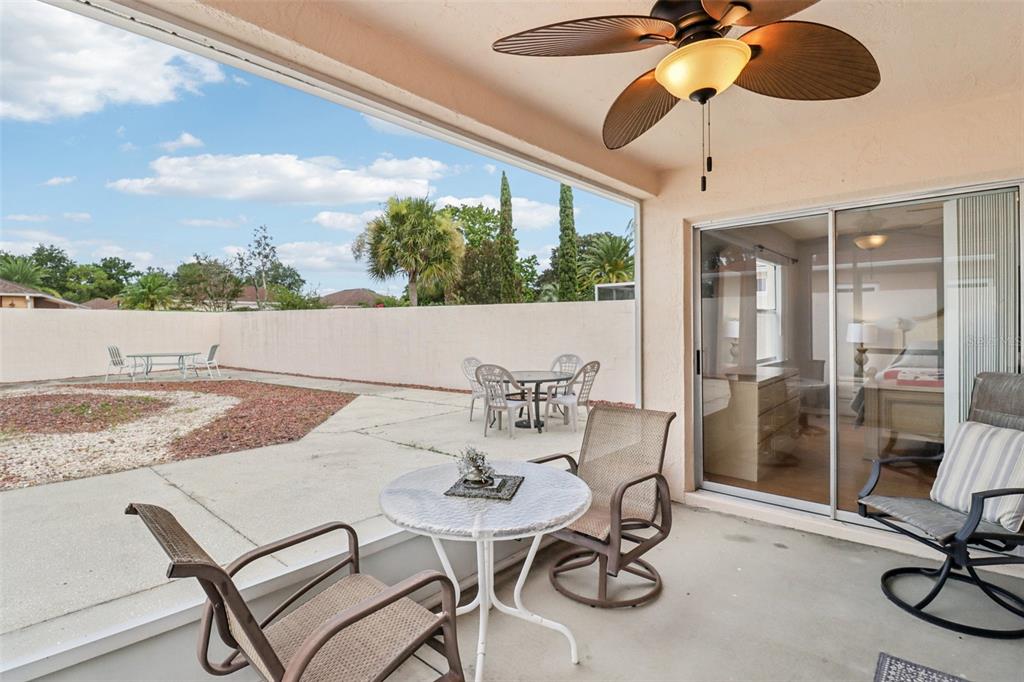 A covered patio with a ceiling fan overlooks a fenced backyard with a concrete patio — 914 MENDOZA BOULEVARD, LADY LAKE, FL