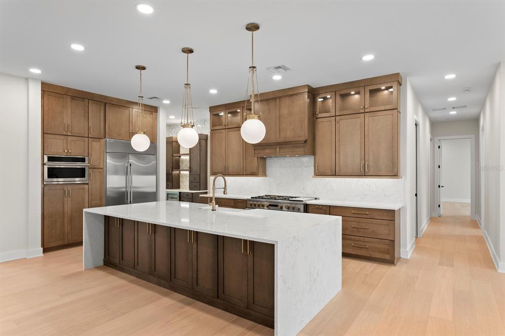 A modern kitchen features wood cabinets, a white quartz waterfall island, and stainless steel appliances — 5021 W LEONA STREET, TAMPA, FL