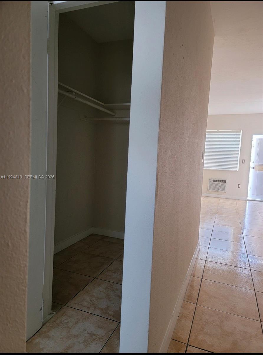 A view of a small closet with a shelf and rod next to a tiled room — 620 76th St # 11, Miami Beach FL 33141, MIAMI BEACH, FL
