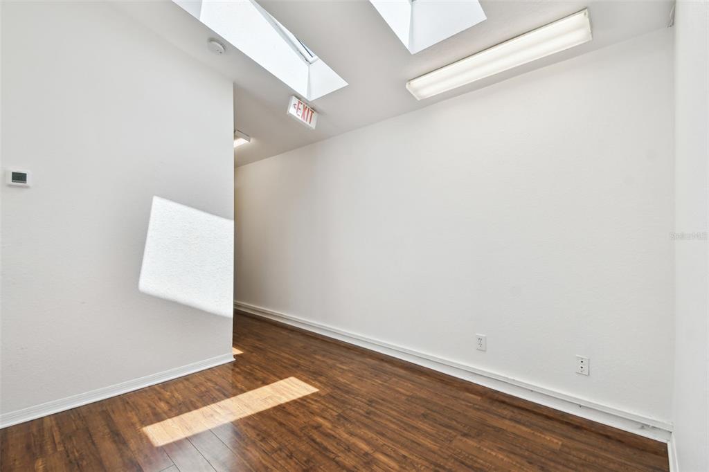 An empty room features wood-look flooring, white walls, a skylight, and an exit sign — 670 2ND STREET N, SAFETY HARBOR, FL