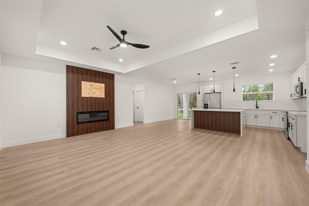 An open-concept living room and kitchen featuring light wood floors and a wood-paneled fireplace — 4225 GERONA AVENUE, SEBRING, FL