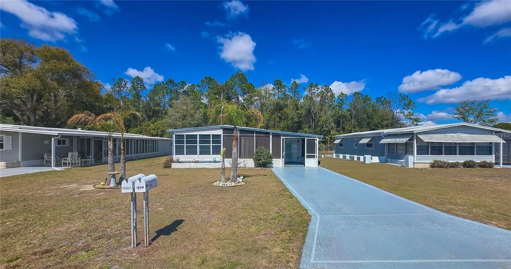 A single-story manufactured home with a screened porch and a blue driveway — 39437 ELGIN DRIVE, ZEPHYRHILLS, FL