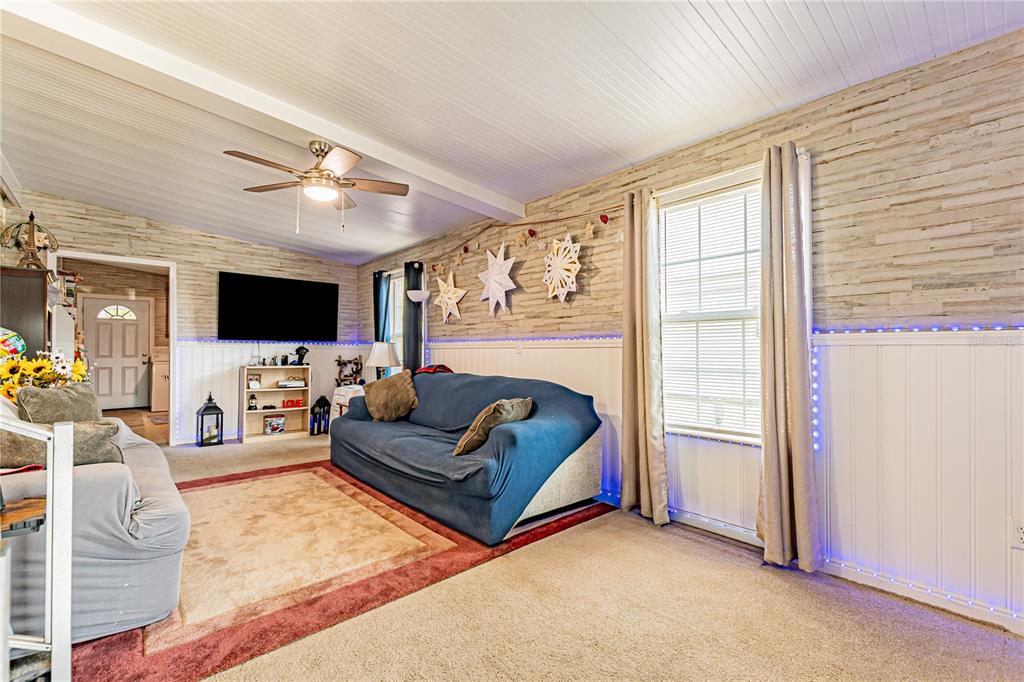 A living room features a blue sofa, beige carpet, wood-paneled walls, and a ceiling fan — 39437 ELGIN DRIVE, ZEPHYRHILLS, FL