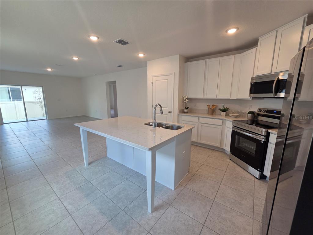 A kitchen features white cabinets, a central island with a sink, and light-colored tile flooring — 2747 SAN MARCO WAY, WINTER HAVEN, FL