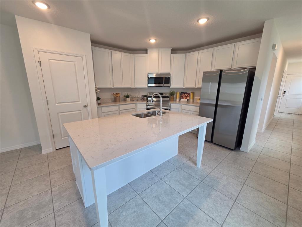 A kitchen features white cabinets, a quartz-topped island with a sink, and stainless steel appliances — 2747 SAN MARCO WAY, WINTER HAVEN, FL