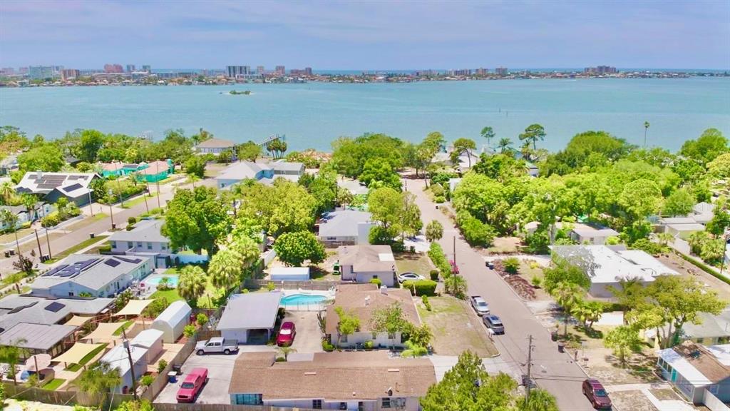 An aerial view shows a residential neighborhood with houses, swimming pools, and a nearby bay — 411 PLEASANT STREET, CLEARWATER, FL