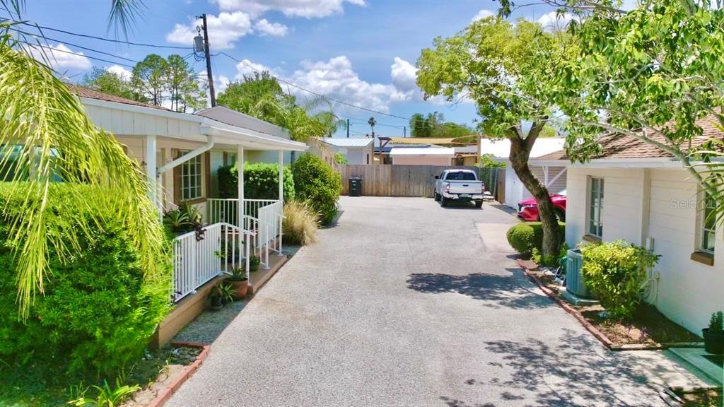 A paved driveway separates two small, light-colored houses with white railings and surrounding greenery — 411 PLEASANT STREET, CLEARWATER, FL
