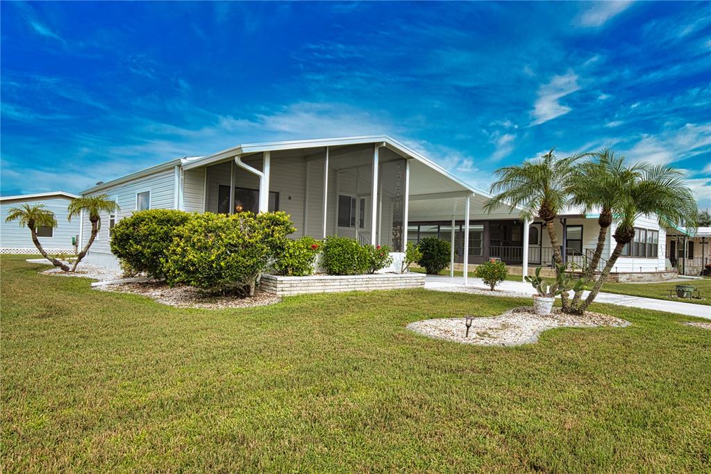 A single-story manufactured home with a screened-in porch, carport, and palm trees on a lawn — 632 LA JOLLA CIRCLE, NORTH PORT, FL