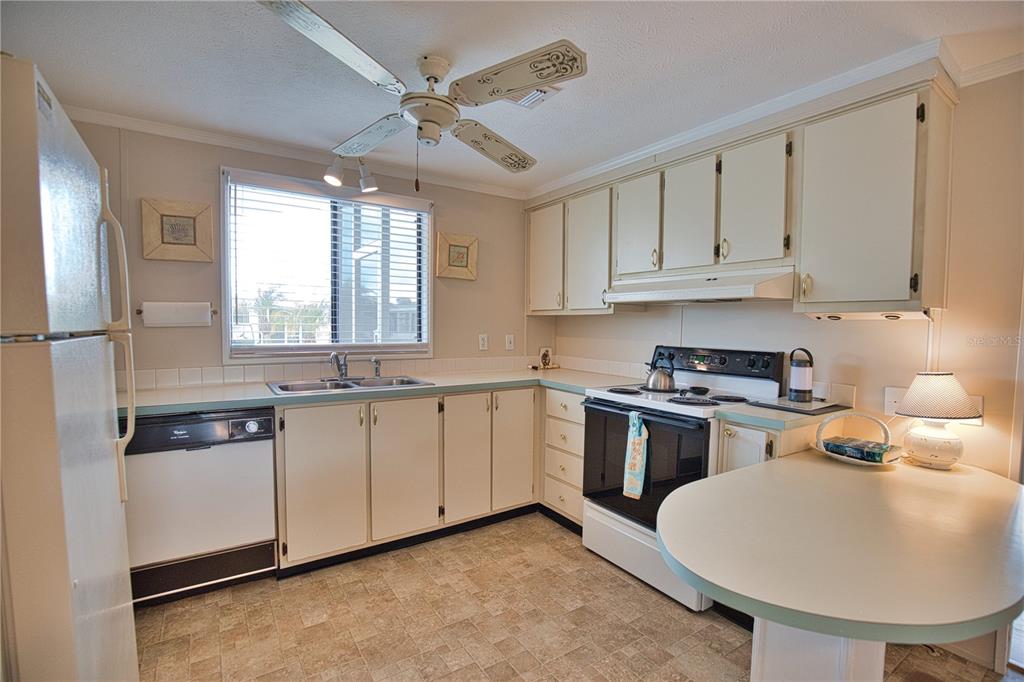 A kitchen with off-white cabinets, a black dishwasher and stove, and a small breakfast bar — 632 LA JOLLA CIRCLE, NORTH PORT, FL