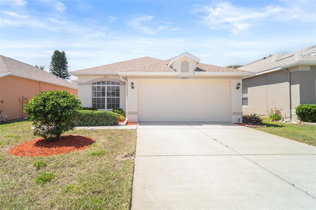A single-story house features a beige exterior, a two-car garage, and a concrete driveway — 2815 WOOD POINTE DRIVE, HOLIDAY, FL