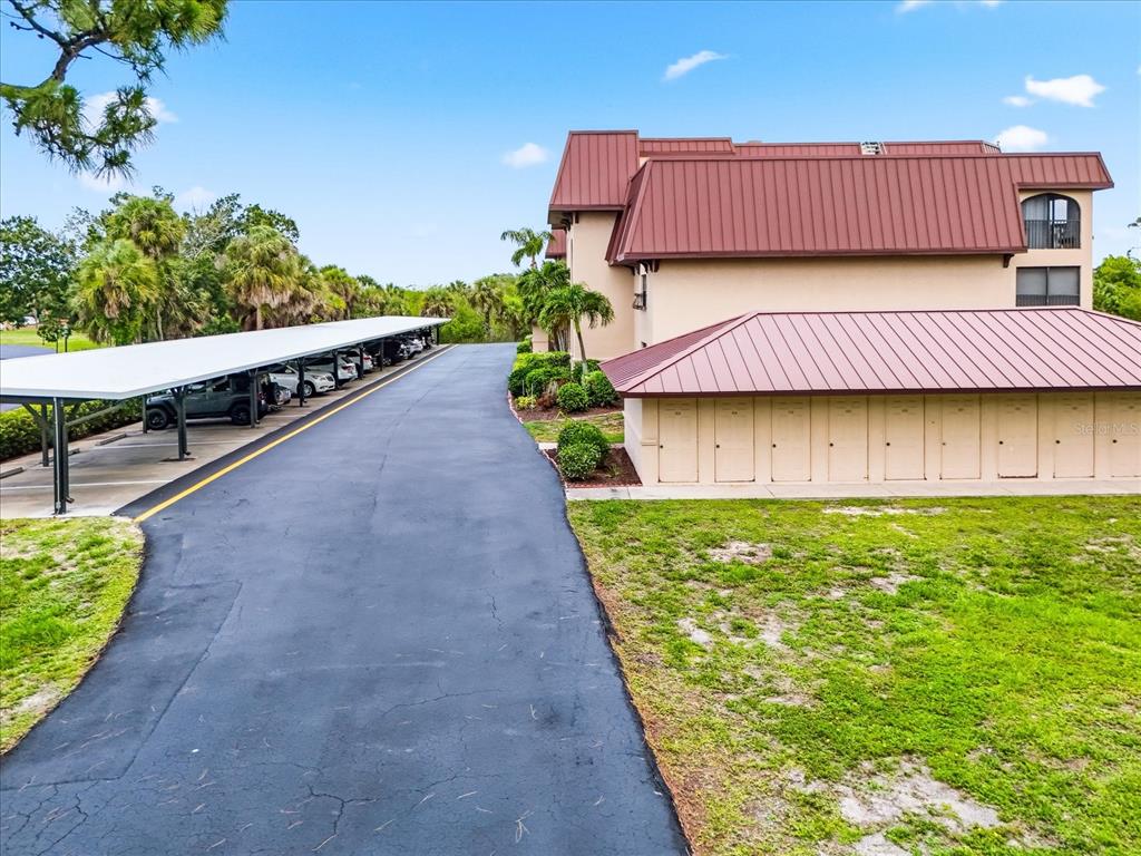 An exterior view of a multi-story building with a metal roof and a covered parking area — 23465 HARBORVIEW ROAD UNIT 235, PUNTA GORDA, FL