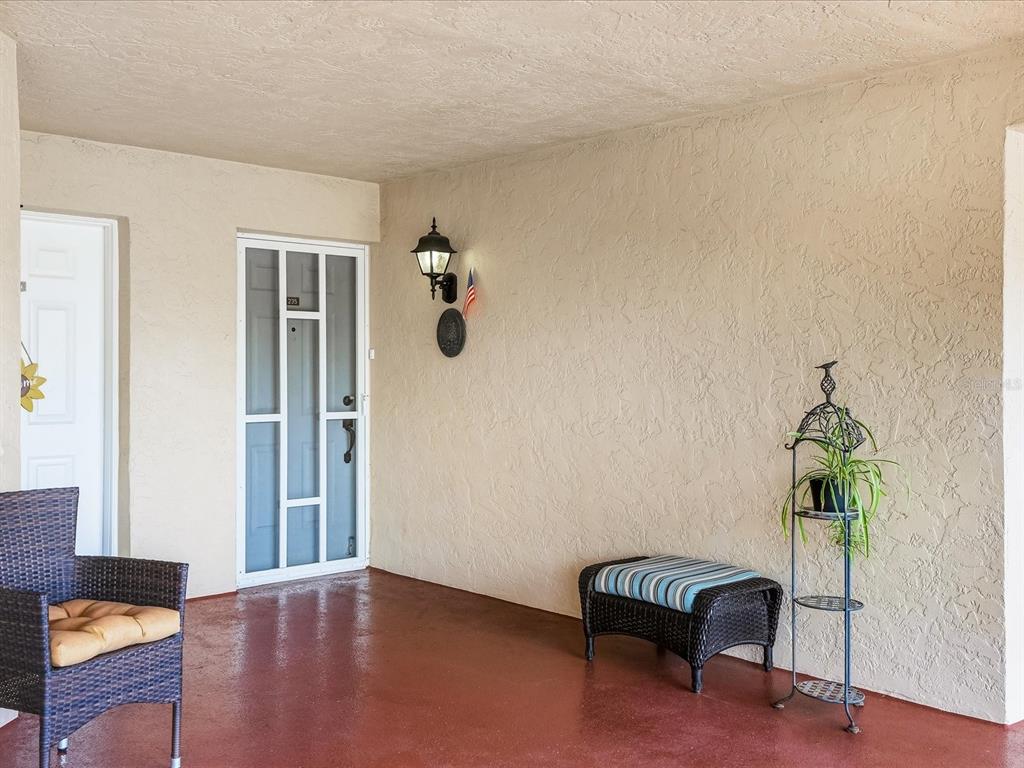 A covered patio features a red floor, a screen door, and wicker furniture — 23465 HARBORVIEW ROAD UNIT 235, PUNTA GORDA, FL