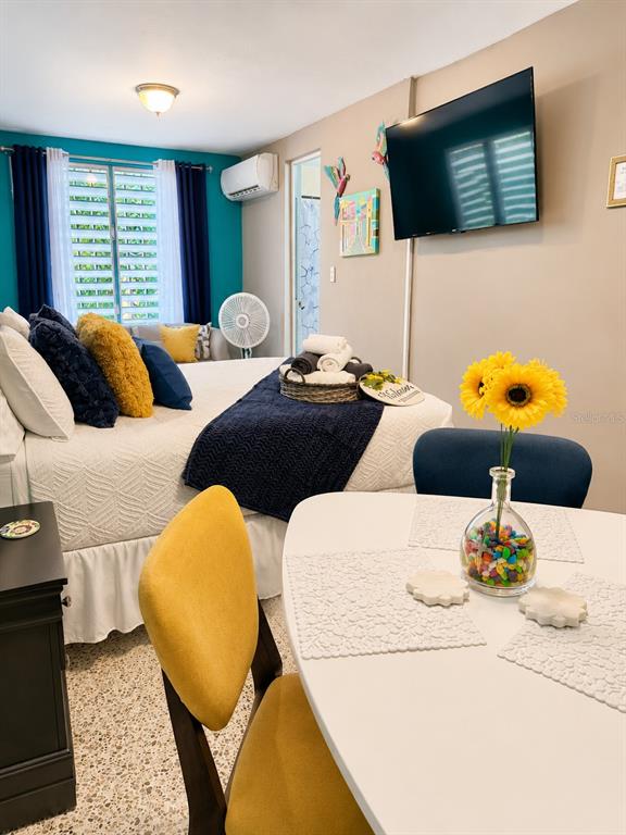 A bedroom features a bed with blue and yellow pillows, a dining table, and a television — CII Via 18 Apt 2 VILLA FONTANA, CAROLINA, PR