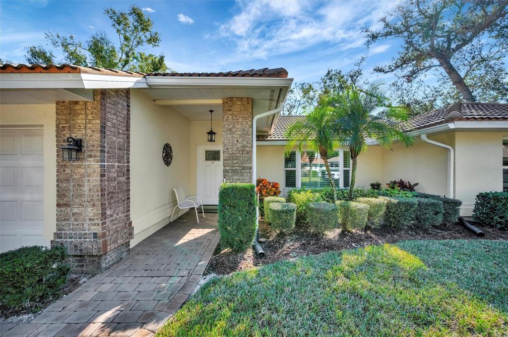 A paved walkway leads to the front entrance of a house with brick accents — 5721 GARDEN LAKES MAJESTIC, BRADENTON, FL