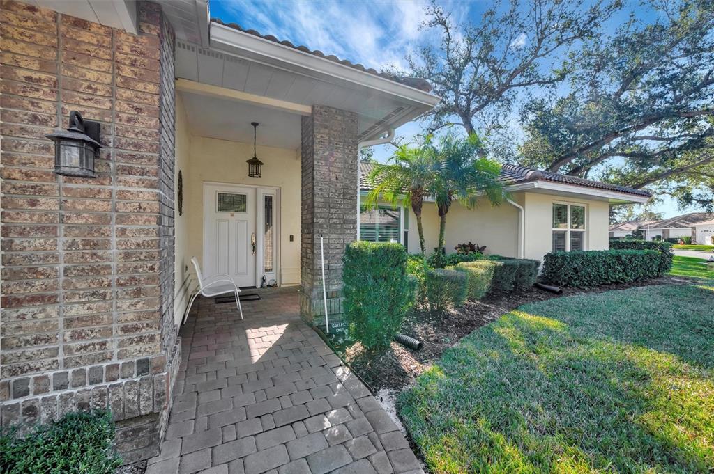 A brick-accented house exterior features a covered entryway, a paved walkway, and manicured landscaping — 5721 GARDEN LAKES MAJESTIC, BRADENTON, FL