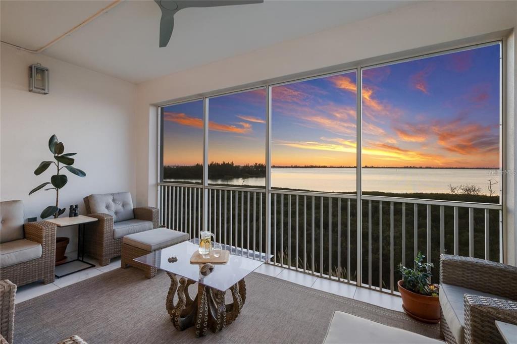 A screened-in balcony features wicker furniture and a glass table overlooking a sunset water view — 376 ARUBA CIRCLE UNIT 203, BRADENTON, FL