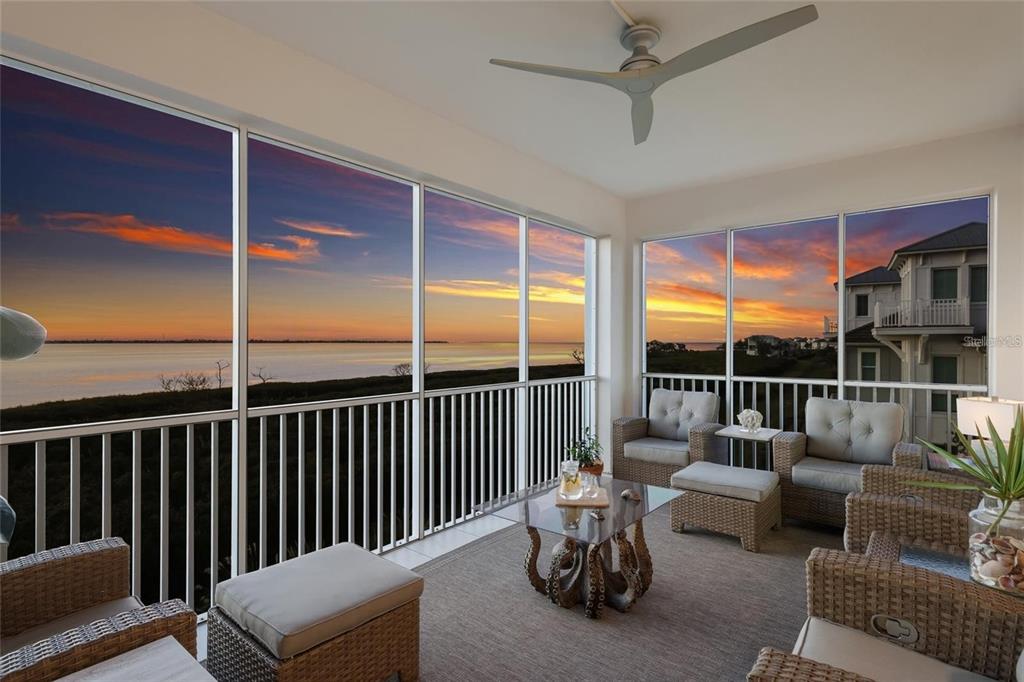 A screened-in porch with wicker furniture overlooks a sunset view of the water — 376 ARUBA CIRCLE UNIT 203, BRADENTON, FL