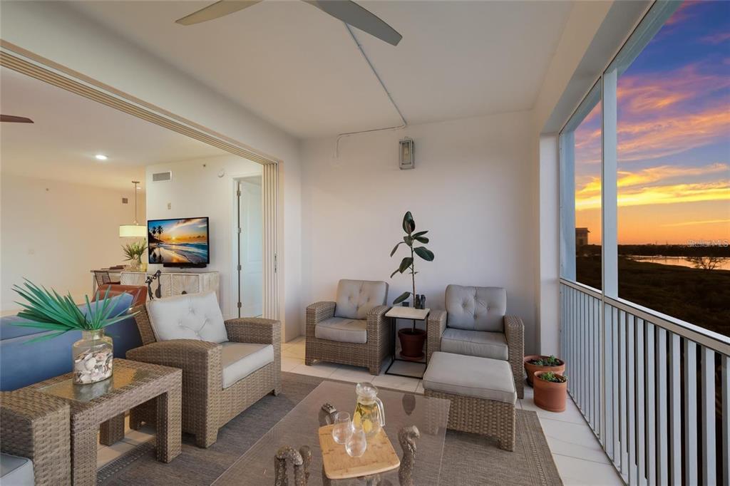 A covered balcony features wicker furniture, a glass coffee table, and a sunset view — 376 ARUBA CIRCLE UNIT 203, BRADENTON, FL